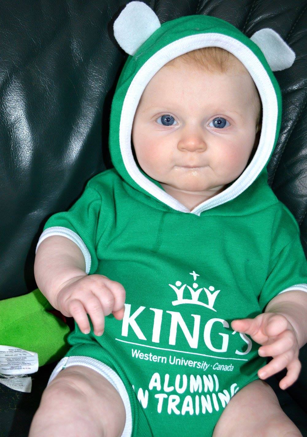 King's College Baby Onesie with Ears. Get your young scholar off to a good start with our baby onsie.  Kelly green with white trim and logo. 100% cotton. Short sleeves. Hood with ears. Opens with snaps at diaper area. Made in Canada.